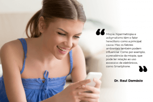 A imagem mostra uma mulher sorrindo enquanto segura um smartphone, vestindo uma blusa azul. Ao lado dela, há uma citação do Dr. Raul Damásio: "Miopia, hipermetropia e astigmatismo têm o fator hereditário como a principal causa. Mas os fatores ambientais também podem influenciar. Como por exemplo, a prevalência da miopia, que pode ter relação ao uso excessivo de eletrônicos, como Smartphone."